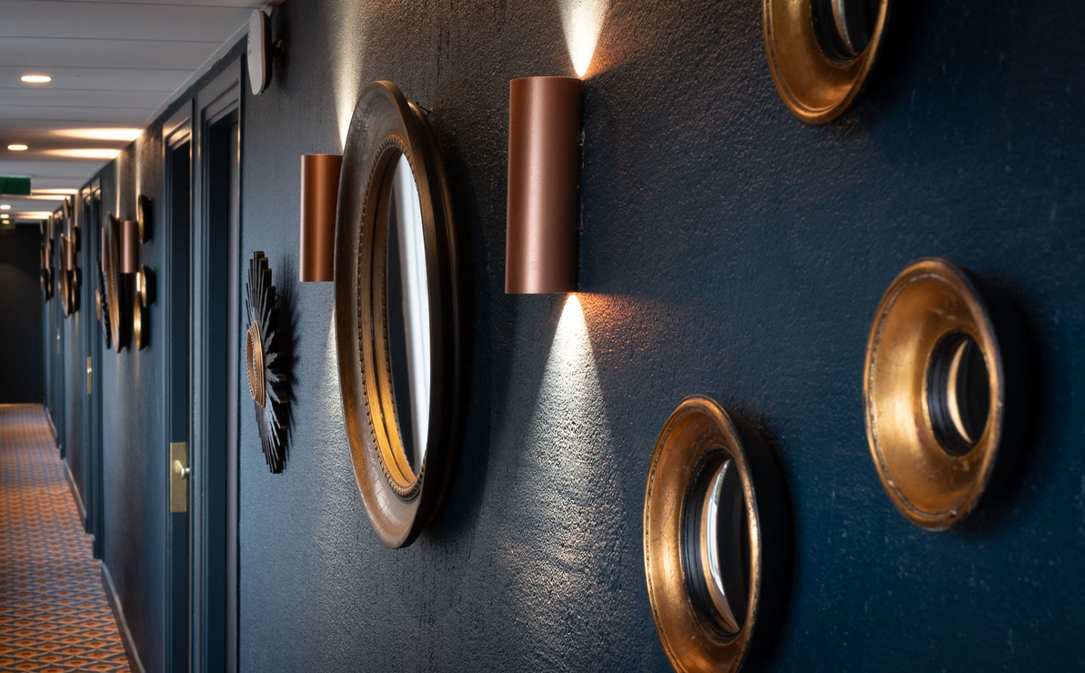 Couloir aux murs bleu nuit, miroirs ronds dor&eacute;s et appliques cuivr&eacute;es